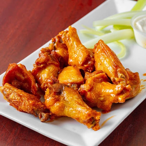 A plate of G's Pizzeria's buffalo wings with celery sticks and ranch dressing.
