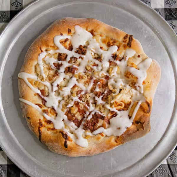 G's Pizzeria's chicken bacon ranch pizza, drizzled with white sauce, on a metal tray.