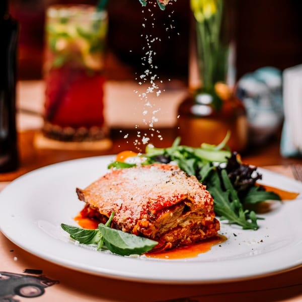 Lasagna with red sauce and cheese, served with a side salad, being sprinkled with parmesan.