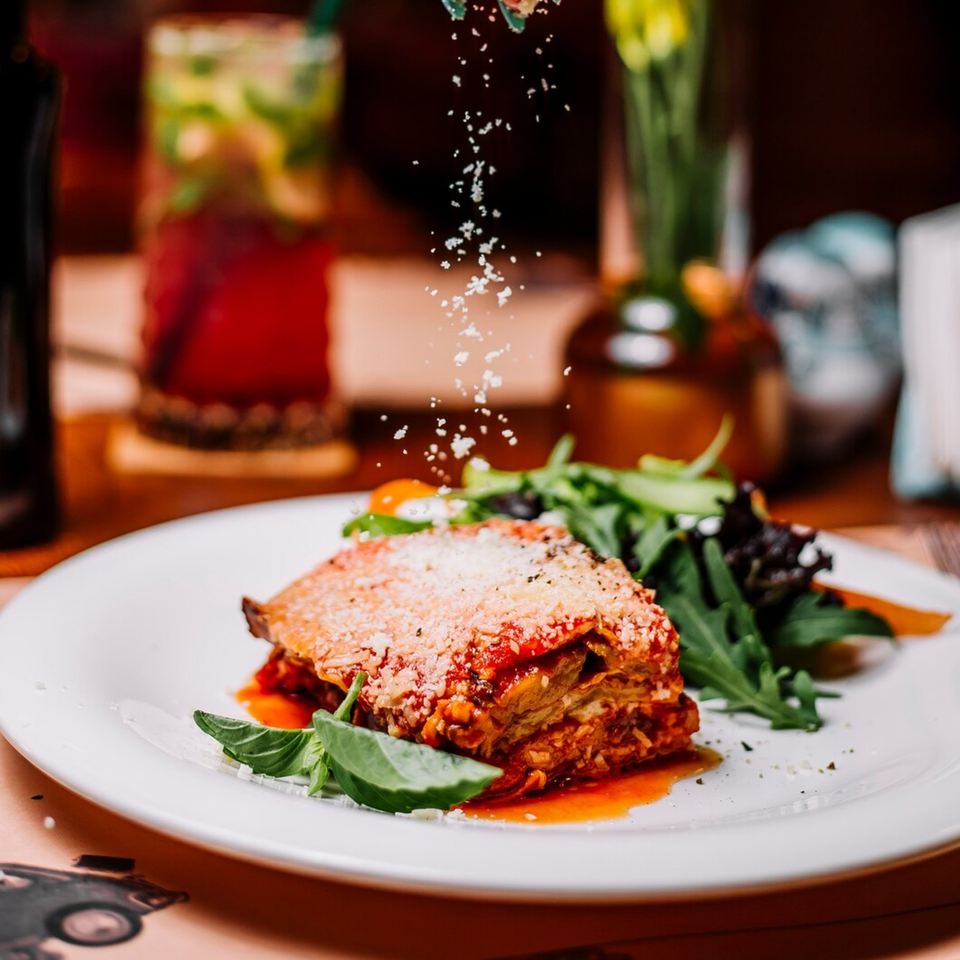 Lasagna with red sauce and cheese, served with a side salad, being sprinkled with parmesan.