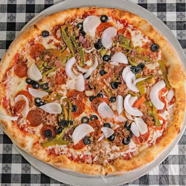 A G's Pizzeria pizza with pepperoni, onions, olives, and green peppers on a checkered tablecloth.